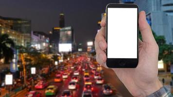 mão masculina segurando um telefone celular com tela branca em branco de toque no fundo da paisagem da cidade turva. foto