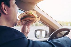 homem dirigindo carro comendo hambúrguer foto