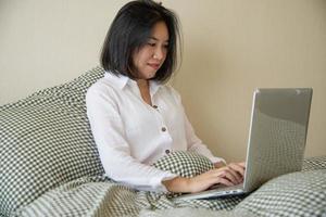 mulher usando computador laptop enquanto acorda na cama de manhã - tecnologia no conceito de vida todos os dias foto