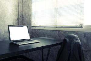 laptop com tela branca em branco sobre a mesa na sala do escritório. tom vintage foto