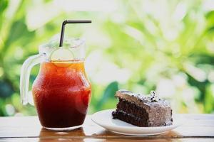 bolo de chocolate na mesa com chá gelado sobre o fundo do jardim verde - relaxe com bebidas e padaria no conceito de natureza foto