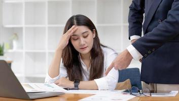 cansada e entediada jovem empresária asiática ou trabalhadora de escritório recebendo uma reclamação de seu chefe masculino no escritório sobre seu desempenho no trabalho. foto