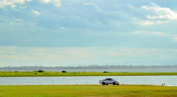 paisagem do lago com uma caminhonete em um monte verde gramado. montanhas distantes o céu está cheio de nuvens negras. conceito de viagens de férias. foto