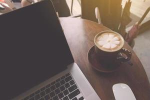 xícara de café e laptop na mesa de madeira na cafeteria. conceito de negócios foto