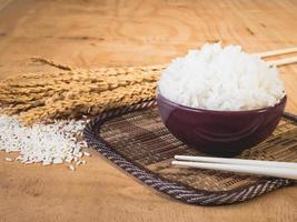 arroz cozido em tigela com grão de arroz cru e planta de arroz seco no fundo da mesa de madeira. foto