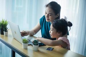 mãe feliz ajudando sua linda filha a estudar online em casa. pai e filho assistindo aula de arte juntos no laptop foto