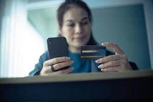 mulher segurando cartão de crédito e usando smartphone no escritório. compras on-line, e-commerce, internet banking, trabalhando em casa. foto