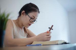 mulher asiática senta-se e faz anotações enquanto estuda a bíblia. conceito de esperança, fé, cristianismo, religião, igreja online. foto