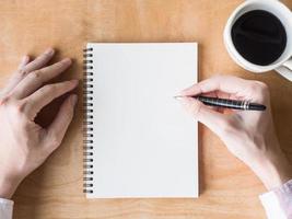 vista superior das mãos masculinas escrevendo alguns dados no notebook, xícara de café na mesa de madeira. foto