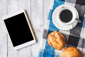 vista superior da xícara de café com pão, toalha de mesa e tablet no fundo da mesa de madeira foto