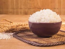 arroz cozido em tigela com grão de arroz cru e planta de arroz seco no fundo da mesa de madeira. foto