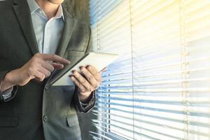 close-up do empresário usando o dispositivo tablet em pé em uma janela em um escritório foto