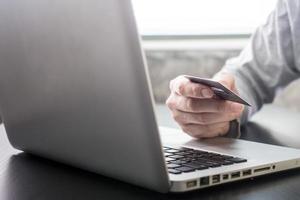 mãos masculinas segurando cartão de crédito e usando laptop, foco suave, conceito de compras online. foto