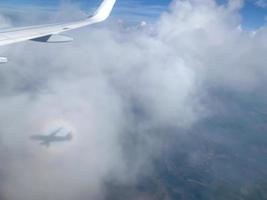 vista da janela do avião nas nuvens com sombra e arco-íris foto