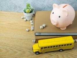 o brinquedo de ônibus escolar e cofrinho na mesa de madeira para voltar à escola ou conceito de educação foto