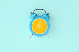 fatia de laranja fresca no pequeno despertador azul foto