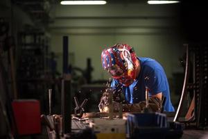 soldador profissional da indústria pesada trabalhando dentro da fábrica, usa capacete e começa a soldar. foco seletivo foto