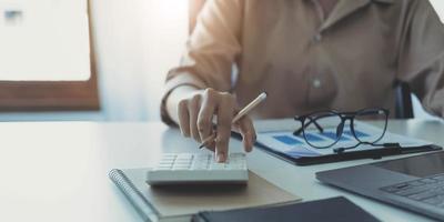 calculadora de imprensa de mão de mulher de close-up para calcular os resultados financeiros da empresa na mesa de madeira no escritório e fundo de trabalho de negócios, impostos, contabilidade, estatísticas e pesquisa analítica. foto