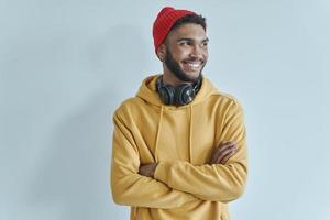 homem africano bonito, mantendo os braços cruzados e sorrindo em pé contra a parede foto