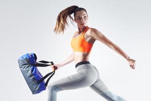 jovem confiante carregando uma bolsa e correndo contra um fundo branco foto