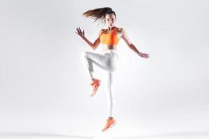 mulher jovem e bonita em roupas esportivas pulando contra fundo branco foto