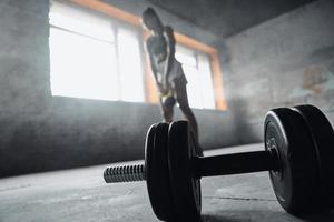 concentrada jovem mulher africana exercitando com kettlebell enquanto haltere deitado em primeiro plano foto