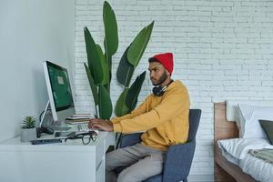 concentrado jovem africano usando computador enquanto está sentado em seu local de trabalho em casa foto