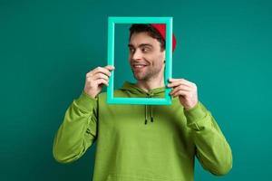 jovem brincalhão olhando através de um porta-retrato em pé contra um fundo verde foto