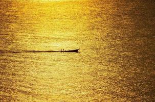 o pôr do sol, a superfície do mar reflete a luz do sol em ouro. o navio corria pela superfície cintilante do mar. foto