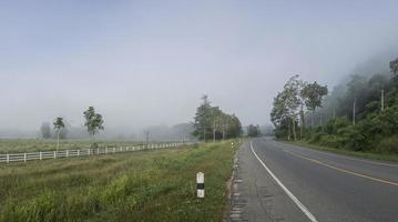 a estrada entre as montanhas e os arrozais cobertos de neblina. a estrada para a vila de pilok, província de kanchanaburi, tailândia. foto