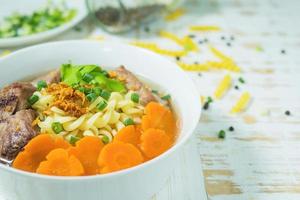 sopa de macarrão com carne de porco e cenoura na mesa de madeira branca - conceito de comida deliciosa e saudável foto