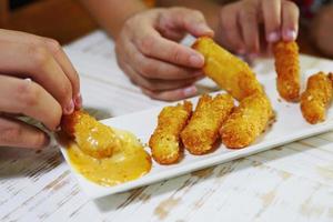 pessoas comendo palito de queijo muitas mãos comendo palito de queijo com molho foto