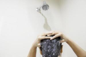senhora usando xampu em um banheiro com água de pulverização do chuveiro foto
