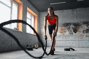 confiante jovem africana se exercitando com cordas de batalha no ginásio foto