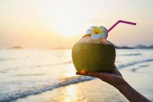 silhueta de coco fresco na mão com plumeria decorada na praia com fundo de ondas do mar - turista com frutas frescas e conceito de fundo de férias de areia do mar foto