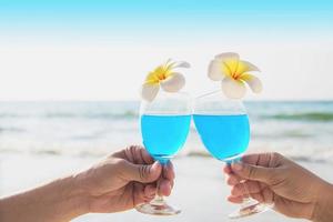 casal asiático segurando decoração de copo de coquetel com flor de plumeria com fundo de praia de mar de ondas - férias de celebração de relaxamento feliz no conceito de natureza do mar foto