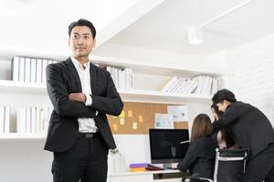 empresário sorrindo feliz em pé com gesto de braços cruzados no escritório durante reunião de negócios. foto