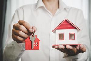 agente imobiliário oferece modelo de casa de mão com chave para cliente e compra ou venda de casa. conceito de empréstimo e seguro de aprovação de empréstimo hipotecário. espaço de cópia