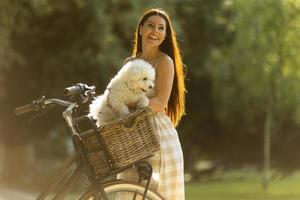 jovem mulher com cachorro branco bichon frise na cesta de bicicleta elétrica foto