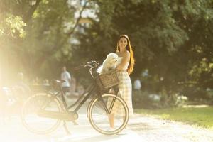 jovem mulher com cachorro branco bichon frise na cesta de bicicleta elétrica foto