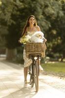 jovem mulher com cachorro branco bichon frise na cesta de bicicleta elétrica foto