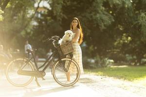 jovem mulher com cachorro branco bichon frise na cesta de bicicleta elétrica foto