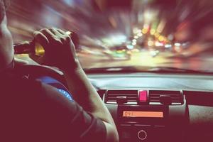 homem bebe cerveja enquanto dirige à noite na cidade perigosamente, sistema de volante à esquerda foto