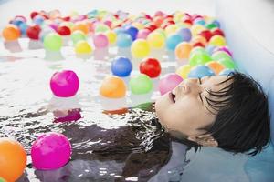 menino brincando com bola colorida em brinquedo de piscina pequena - menino feliz no conceito de brinquedo de piscina de água foto