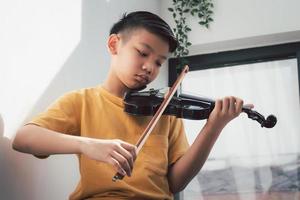 uma criança asiática tocando e praticando violino instrumento musical de cordas contra em casa, conceito de educação musical, inspiração, estudante de escola de arte adolescente. foto