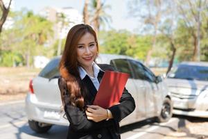 mulheres asiáticas são agentes de seguros segurando pranchetas e em pé na frente de acidentes de carro depois de verificar danos no carro, conceitos de seguro e acidentes de trânsito. foto