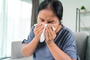 mulher doente fria tem tosse de alergia no nariz ou espirro com lenço de papel sentado no sofá. cuidados de saúde e conceito médico. foto
