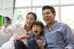 família asiática assistindo tv juntos no sofá na sala de estar. família e casa foto