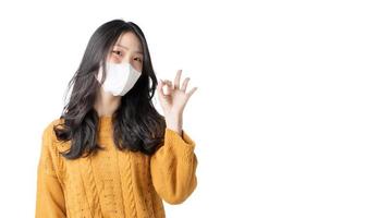 jovem asiática usa máscara facial e mostra gesto bem em isolar fundo branco foto