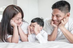 retrato família feliz mãe pai e filho sorrindo no quarto de cama. olhem uns para os outros. foto